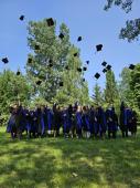 Grupa uśmiechniętych studentów ubranych w czarne togi wyrzuca birety w górę po odebraniu dyplomów